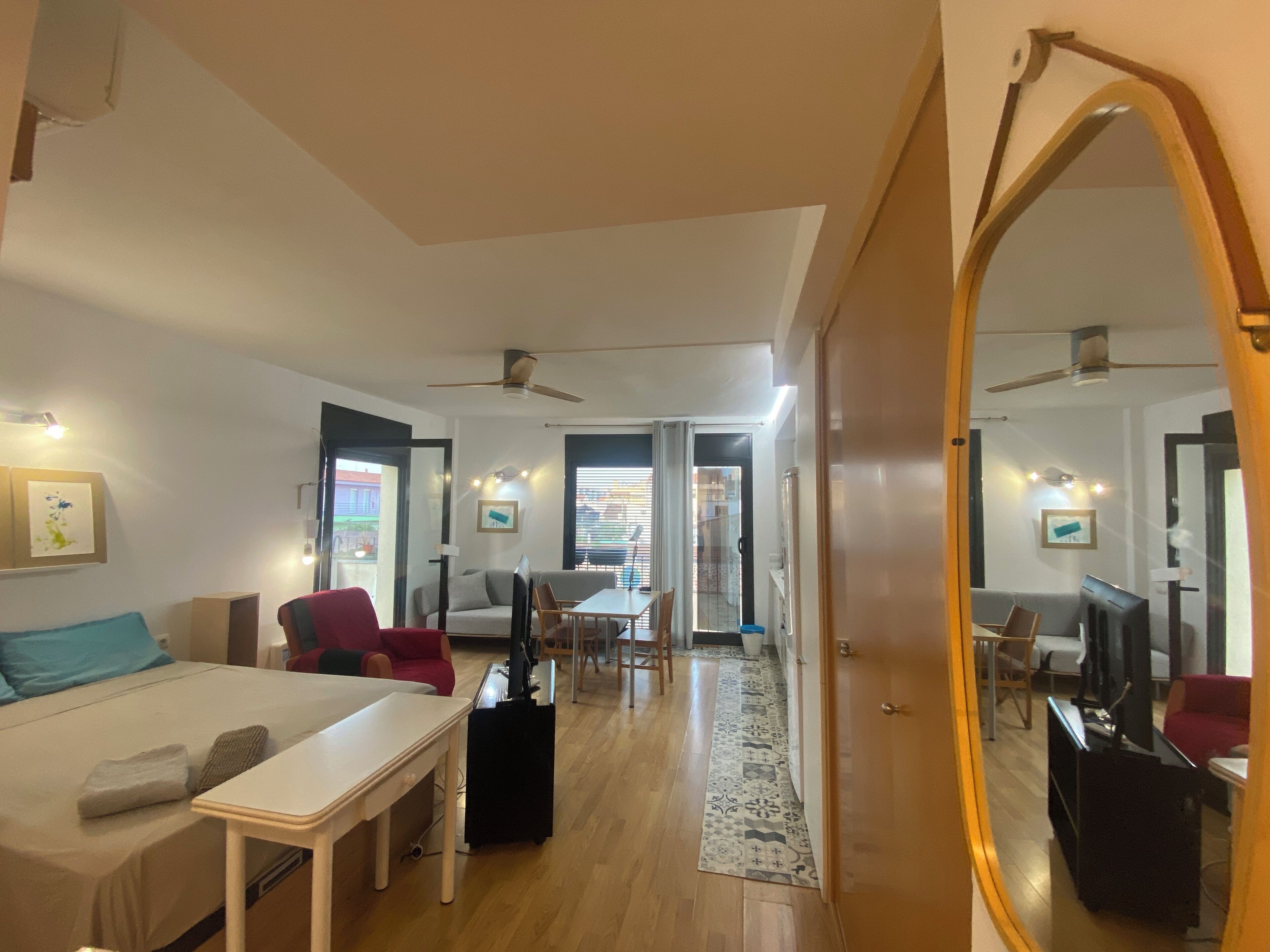 A modern hotel room with a bed, a desk, a TV, and a dining area with chairs and a table.