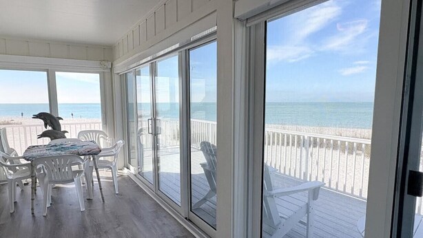 Un espacio al aire libre cubierto con una mesa y sillas, vista a la playa y una terraza de madera.