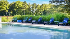 A poolside area with lounge chairs and a small table, surrounded by greenery and trees. - Juniper Presents: The Loft at Historic 33 Acre Berrywood Farm (Three Oaks)