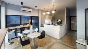 A modern cafe with round tables, black and white chairs, a white counter with a coffee machine, and pendant lighting. - Wan Residence Ratchatewi  (Bangkok)