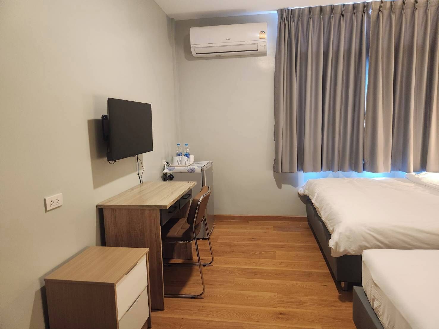 Quarto de hotel com cama, escrivaninha com cadeira, televisão e ar condicionado.