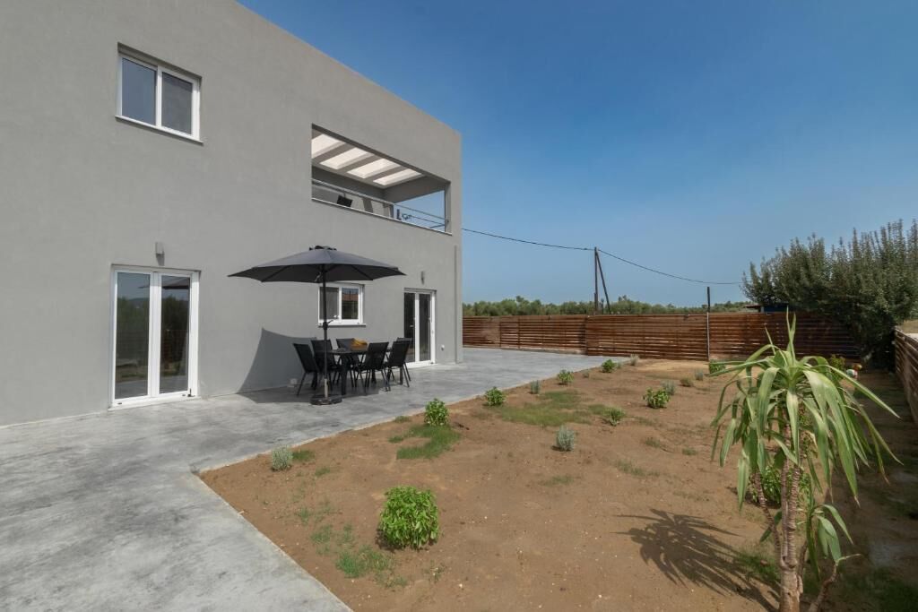 Et moderne hus med to etager og en terrasse med et bord og stole under en stor parasol.