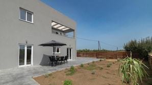 Ein modernes, zweistöckiges Haus mit einer Terrassenanlage, inklusive Tisch und Stühlen unter einem großen Sonnenschirm.
