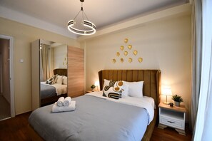A hotel room with a large bed, a mirror, a wooden headboard, a bedside table with a lamp, and decorative leaf wall art. - Porto Sea View Apartments - Tsimiski 78 (Thessaloniki)