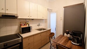 A compact kitchen with a microwave, stove, sink, and wooden table with chairs. - Porto Sea View Apartments - Tsimiski 78 (Thessaloniki)