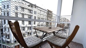A balcony with a wooden table and two cushioned chairs, overlooking a cityscape with multiple buildings. - Porto Sea View Apartments - Tsimiski 78 (Thessaloniki)