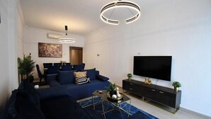 A modern living room with a dark blue sofa, a flat-screen TV, and a minimalist black entertainment unit. - Porto Sea View Apartments - Tsimiski 78 (Thessaloniki)