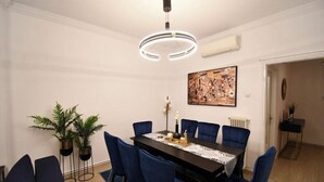 A dining room with a dark wooden table, blue upholstered chairs, and a modern pendant light. - Porto Sea View Apartments - Tsimiski 78 (Thessaloniki)