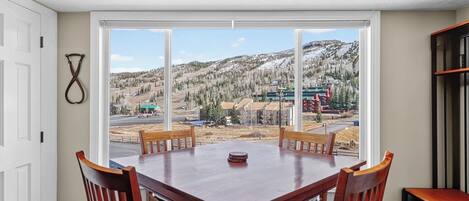 A dining area with a large table and chairs, a view of a snowy mountain landscape, and a door to the left.