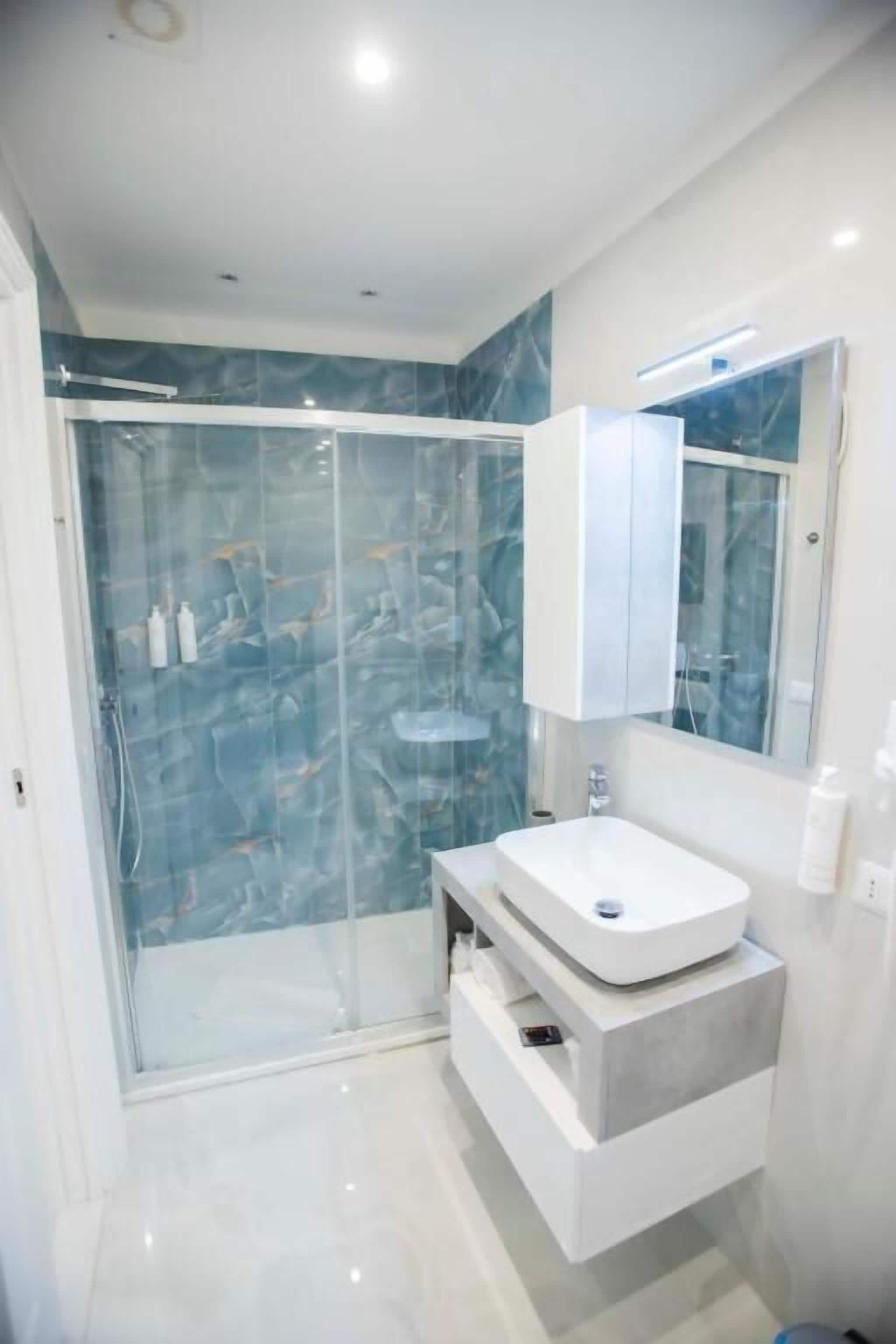 A modern bathroom with a glass-enclosed shower, a white vanity with a marble countertop, and a large mirror above the sink.