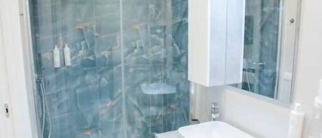 A modern bathroom with a glass-enclosed shower, a white vanity with a marble countertop, and a large mirror above the sink.
