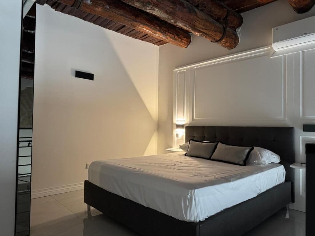 Une chambre avec un grand lit, une poutre en bois au plafond et une table de chevet avec une lampe.