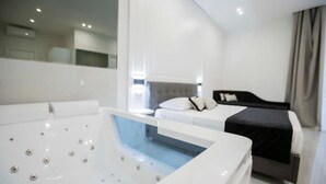 A modern hotel room with a large white bathtub, a bed with black and white bedding, and a view of the city through large windows. - Gentile Suite Decumani (Naples)