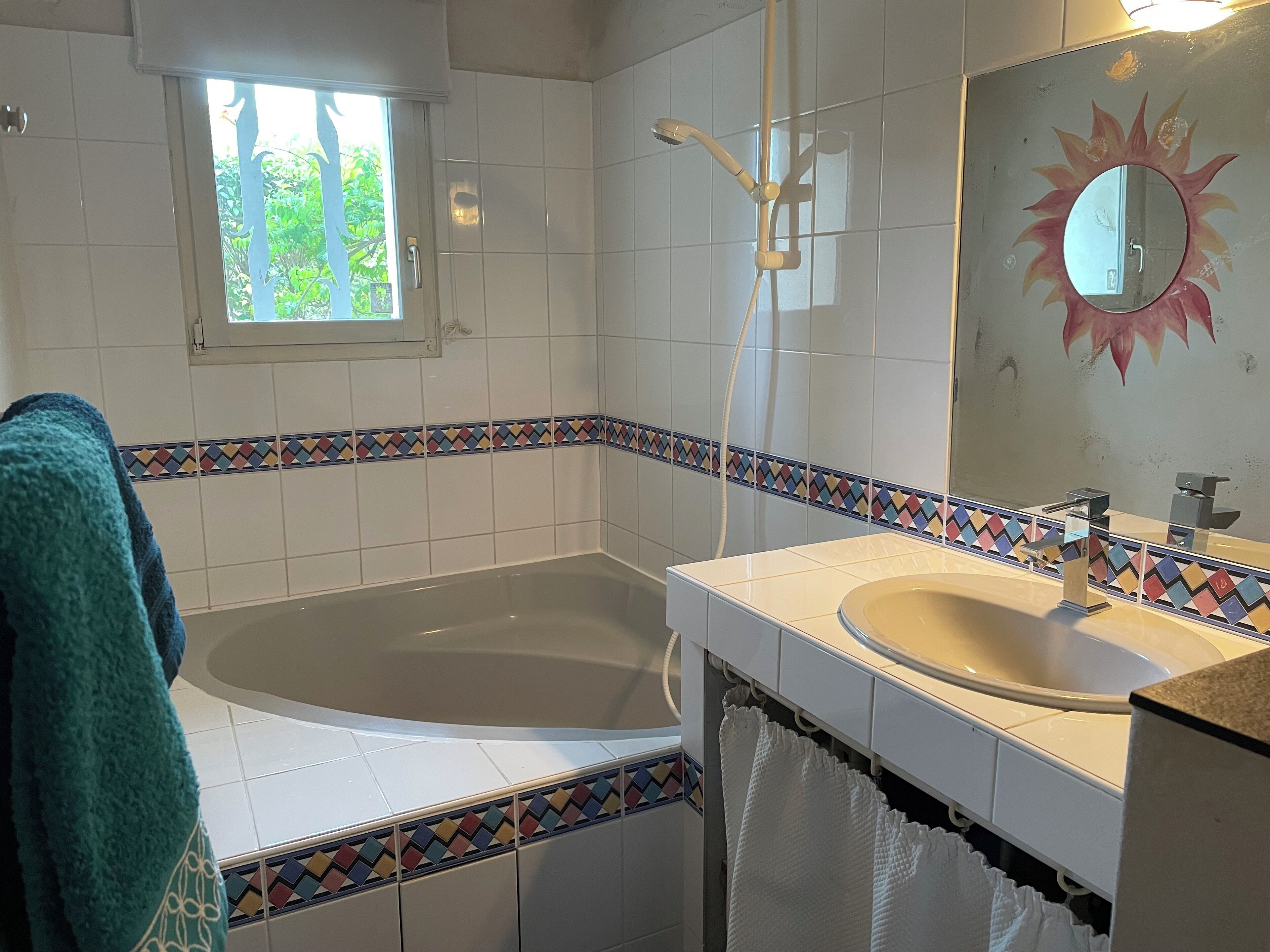 A bathroom with a bathtub, a sink, a window, and a mirror with a sun design.
