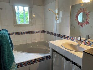 Ett badrum med badkar, handfat, fönster och en spegel med solmotiv.