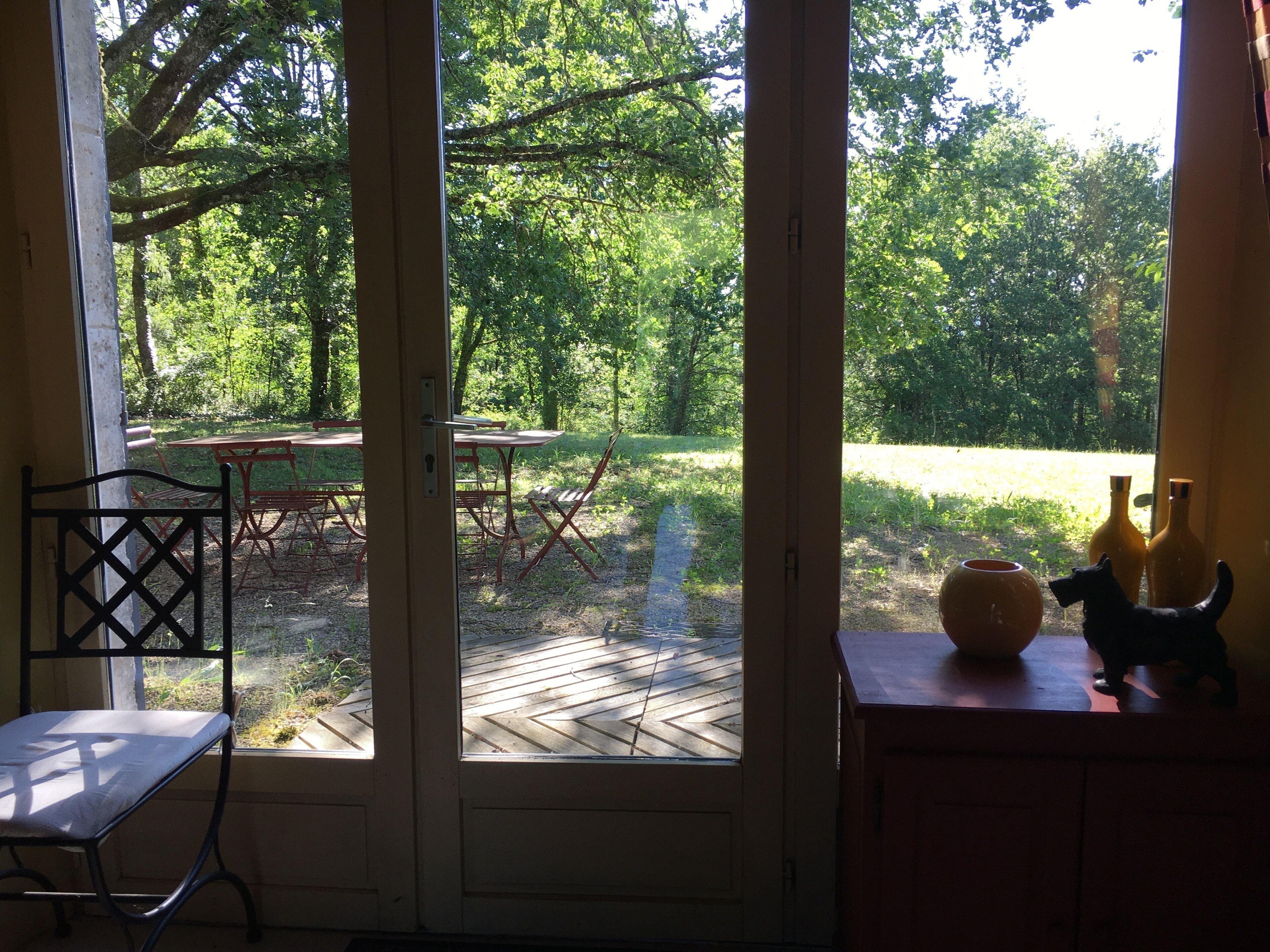 A view through a glass door into a backyard with a wooden deck, outdoor furniture, and a small garden.