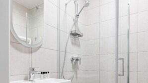 Een moderne badkamer met een douchecabine van glas, een houten wastafelmeubel en een ronde spiegel.