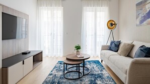 A modern living room with a flat-screen TV, a round coffee table with a plant, a sofa with cushions, and a floor lamp. - D52/3 one bedroom apartment (Budapest)