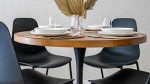 A round dining table with a vase of dried leaves, surrounded by black chairs. - D52/3 one bedroom apartment (Budapest)