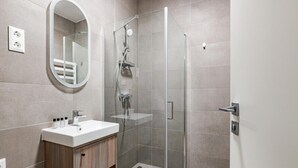 Un baño moderno con ducha envuelta en vidrio, tocador de madera y un espejo grande.