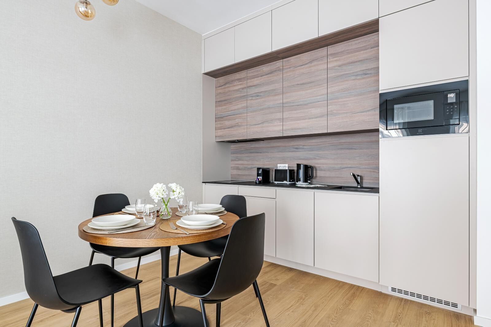 A modern kitchen with white cabinets, a built-in microwave, and a dining area with a round table and black chairs.