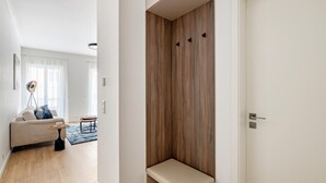 Una sala de estar moderna con un sofá, una mesa de centro y una lámpara. Hay un banco de madera en la esquina y una puerta a la derecha.