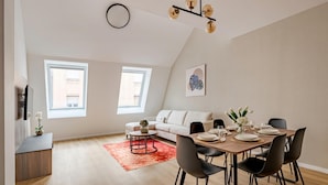 Una sala de estar moderna con comedor, que incluye un sofá, una mesa de comedor preparada para cuatro personas y una alfombra roja.