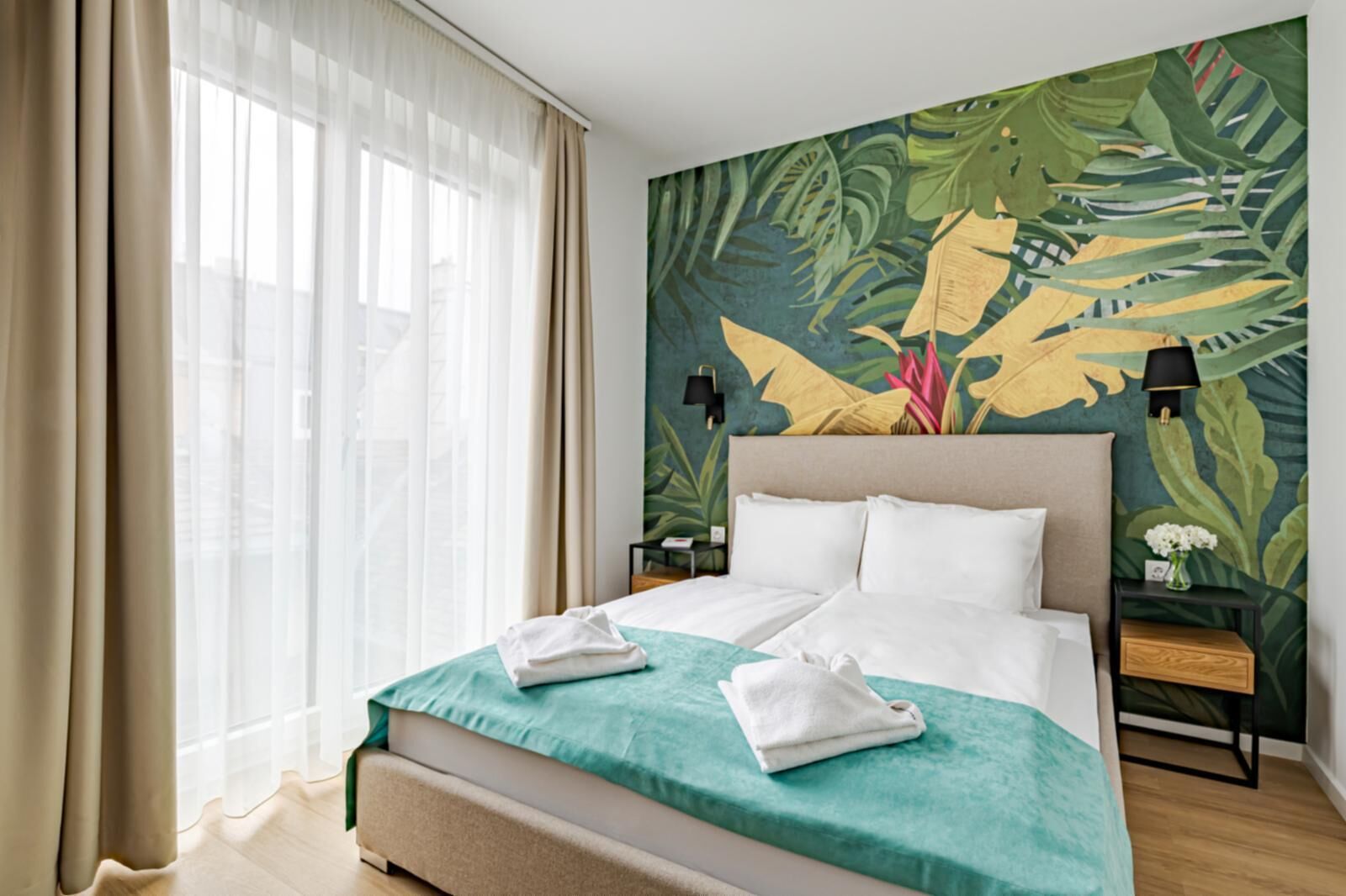 A hotel room with a bed, a nightstand, a lamp, and a large window with curtains.