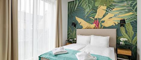 A hotel room with a bed, a nightstand, a lamp, and a large window with curtains.