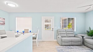 Una sala de estar moderna con un sofá gris, una zona de comedor con una mesa y sillas blancas, y una mesita redonda con una planta.