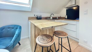 A modern kitchen with a wooden countertop, two stools, a blue chair, and a window. - 4★ Bright Studio on Top Floor, Wifi, 5 min Walk to Quimper Station (Quimper)