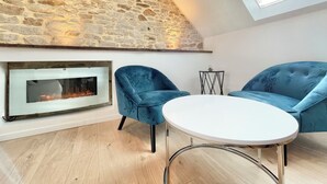 A cozy room with a stone wall, a fireplace, two blue armchairs, and a small table. - 4★ Bright Studio on Top Floor, Wifi, 5 min Walk to Quimper Station (Quimper)