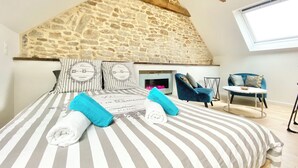 A bedroom with a stone ceiling, a bed with striped bedding, and a view of a blue chair and table. - 4★ Bright Studio on Top Floor, Wifi, 5 min Walk to Quimper Station (Quimper)