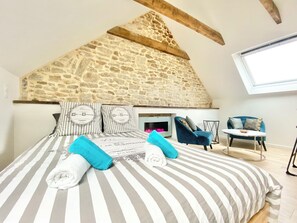 A bedroom with a stone ceiling, a bed with striped bedding, and a view of a blue chair and table. - 4★ Bright Studio on Top Floor, Wifi, 5 min Walk to Quimper Station (Quimper)