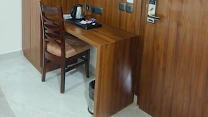 A compact room with a wooden desk, a chair, a television mounted on the wall, and a small trash bin. - Navya Residency  (Jaipur)