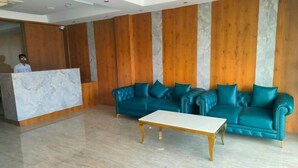 A reception area with a marble reception desk, teal leather sofas, and a white coffee table. - Navya Residency  (Jaipur)