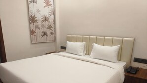 A neatly made bed with a headboard, a bedside table with a phone, and a wall with a palm tree pattern. - Navya Residency  (Jaipur)