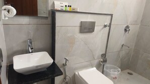 A bathroom with a white sink, a toilet, and a shower. There is a towel rack and a soap dispenser on the wall. - Navya Residency  (Jaipur)