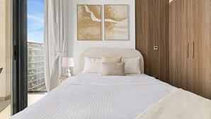 A modern bedroom with a large bed, a wooden wardrobe, and two abstract paintings on the wall. - Bright Modern Studio in Meydan (Dubai)