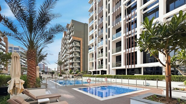 A modern outdoor pool area with lounge chairs and a palm tree. - Bright Modern Studio in Meydan (Dubai)