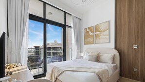 A modern hotel room with a large bed, a desk, and a view of the cityscape through floor-to-ceiling windows. - Bright Modern Studio in Meydan (Dubai)