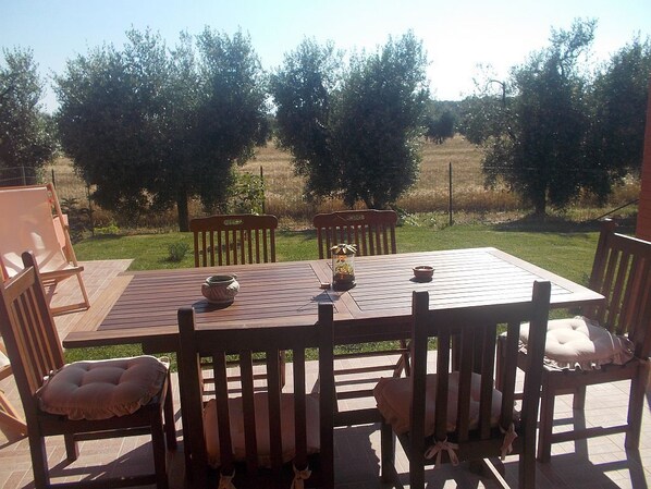 An outdoor wooden table and chairs set on a patio with a view of trees and a grassy field. - Appartamento Girasole (San Vincenzo)