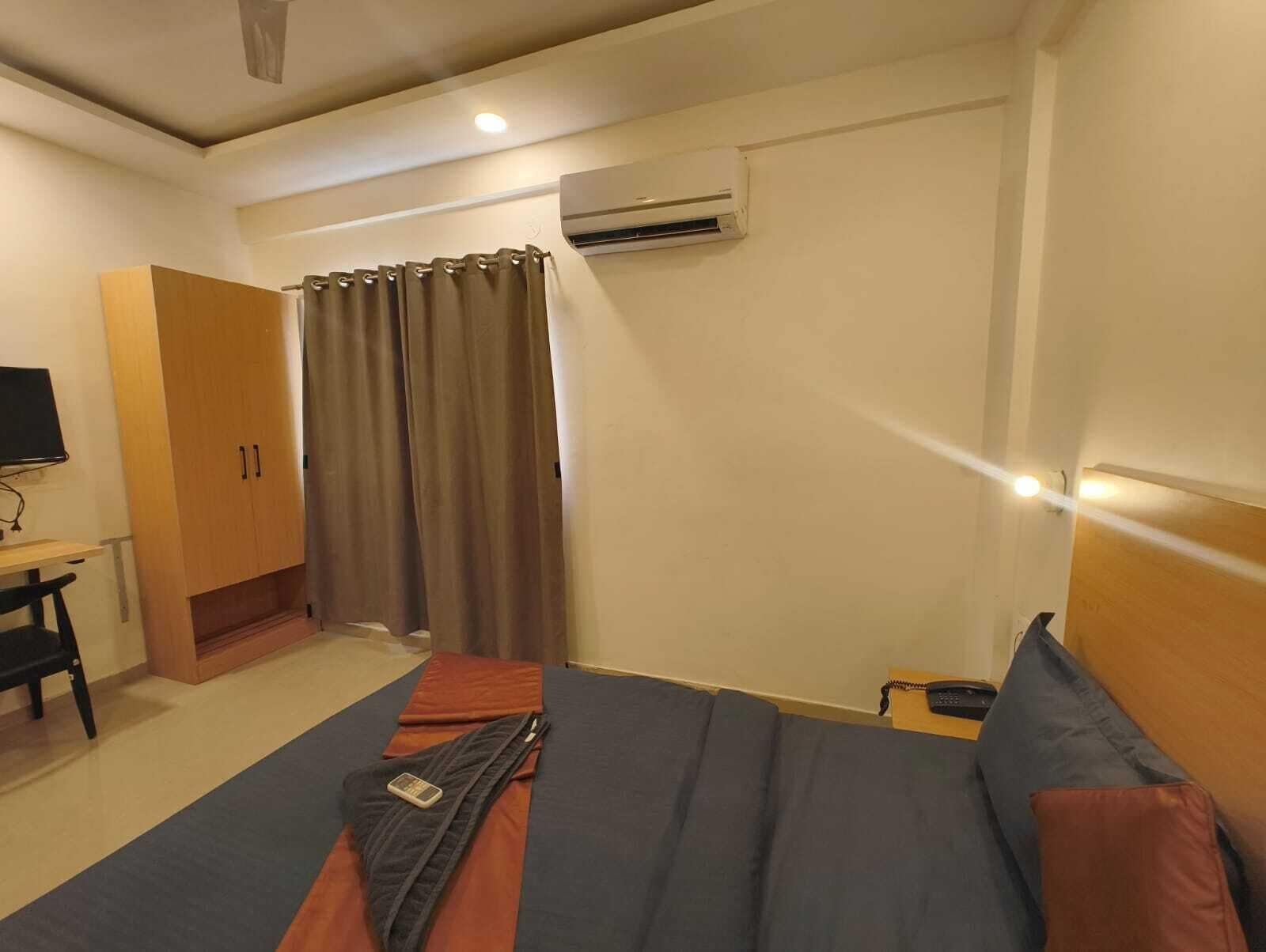 A hotel room with a bed, a desk, a chair, an air conditioning unit, and a television.