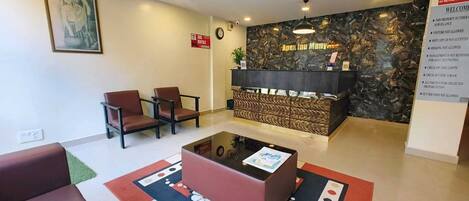 A reception area with a reception desk, two brown chairs, a red sofa, and a patterned rug.
