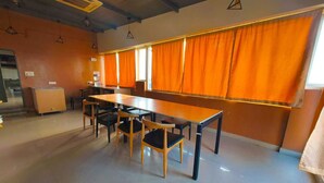 A spacious room with a long table and chairs, orange curtains, and a tiled floor. - Apex Inn Manyata (Bengaluru)