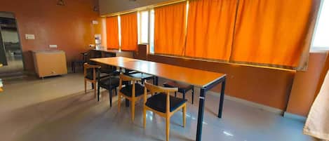 Una habitación amplia con una mesa larga y sillas, cortinas naranjas y suelo de baldosas.