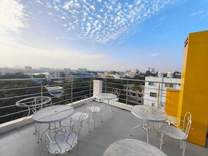 A rooftop terrace with round tables and metal chairs, overlooking a cityscape with buildings and greenery. - Apex Inn Manyata (Bengaluru)