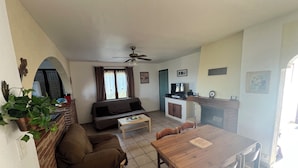 Un espace de vie compact comprenant un canapé, une table à manger, un téléviseur et un ventilateur de plafond.