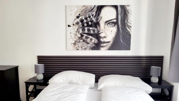 A double bed with white linens, two bedside tables with lamps, and a large abstract painting on the wall. - City Home Lifestyle Vienna (Vienna)