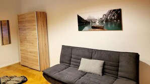 A modern living room with a grey sofa, a wooden cabinet, and a painting of a mountain lake. - City Home Lifestyle Vienna (Vienna)